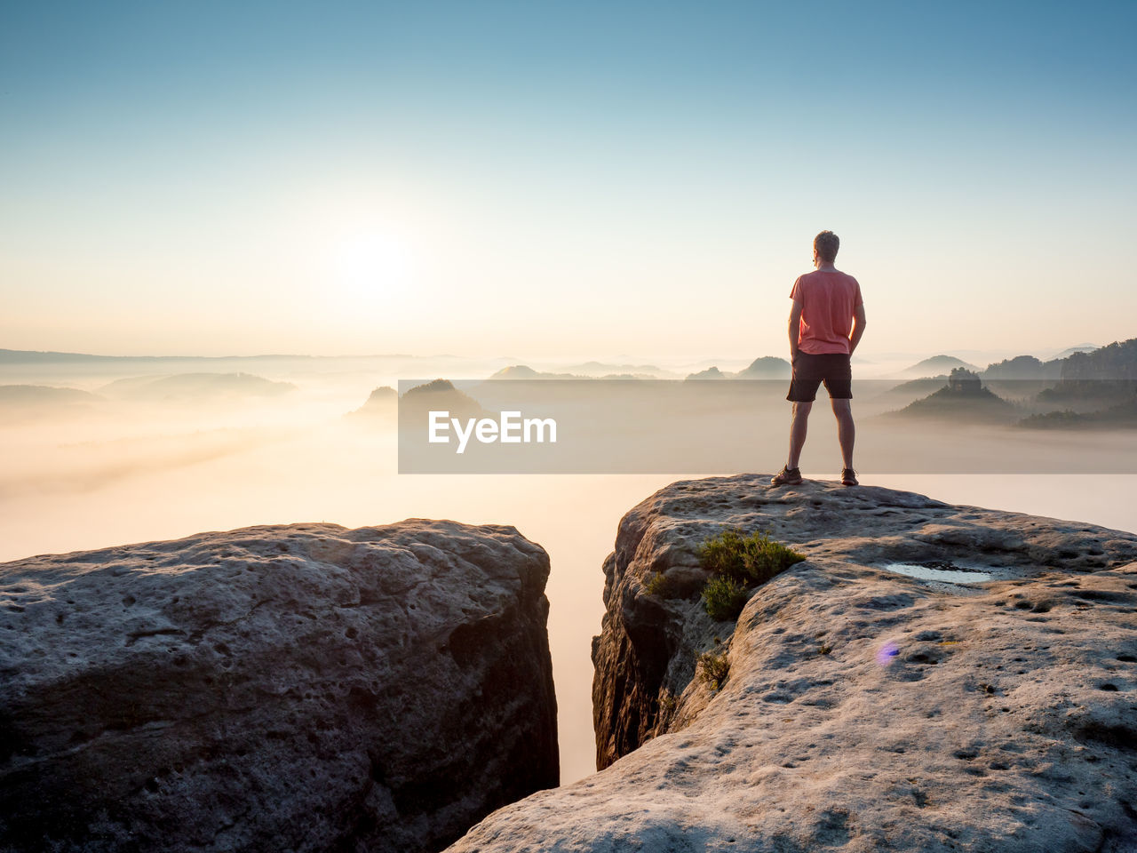 Tourist or hiker on the peak of high rocks watching morning mist in landscape. sport and active life