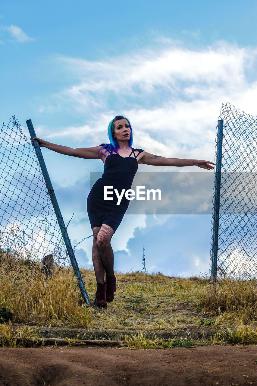 Woman standing by damaged gate against sky