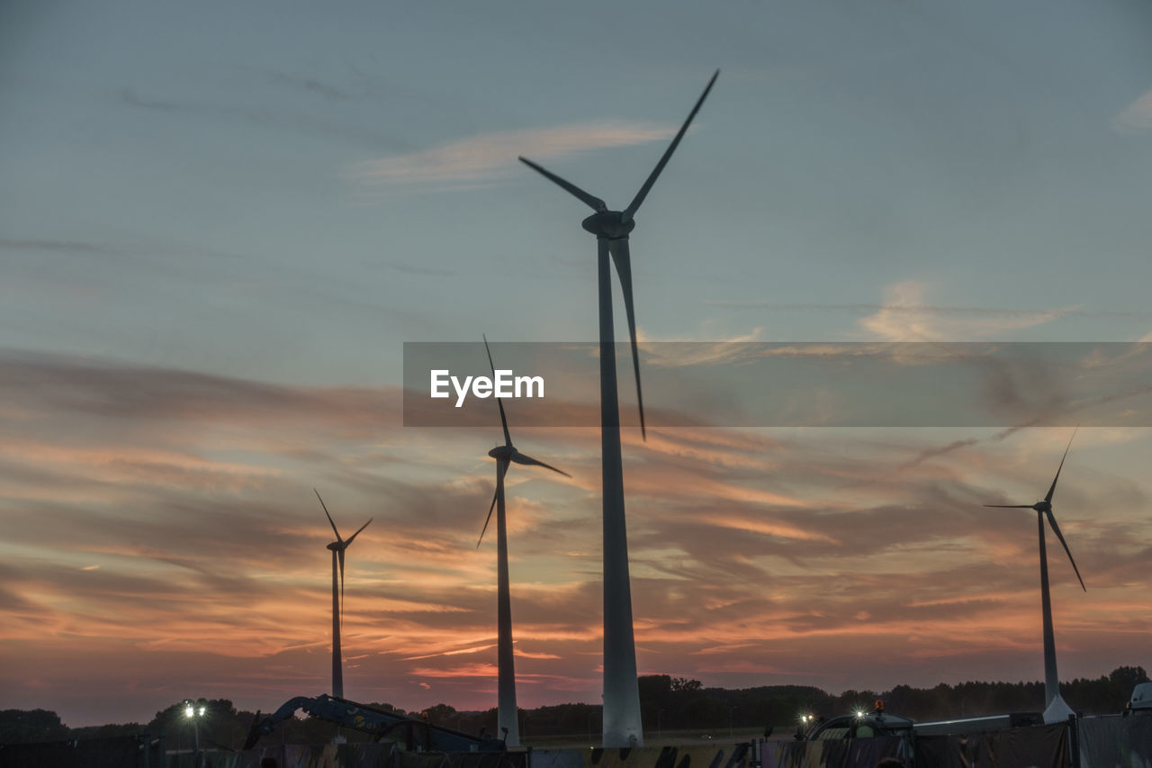 Silhouette wind turbines on landscape against sky at sunset