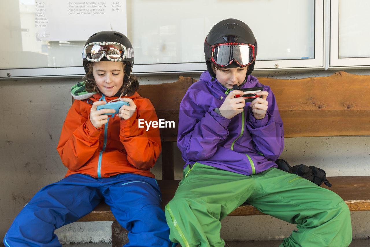 Brother and sister in skiing clothes using cell phones