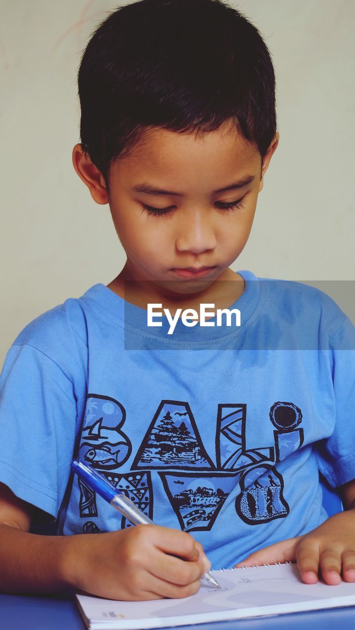 CLOSE-UP OF BOY HOLDING CAMERA AGAINST WALL AGAINST WHITE BACKGROUND