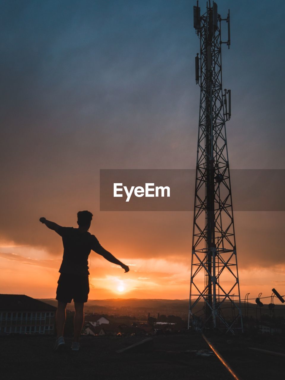 Rear view of silhouette young man with arms outstretched standing on field against cloudy sky during sunset