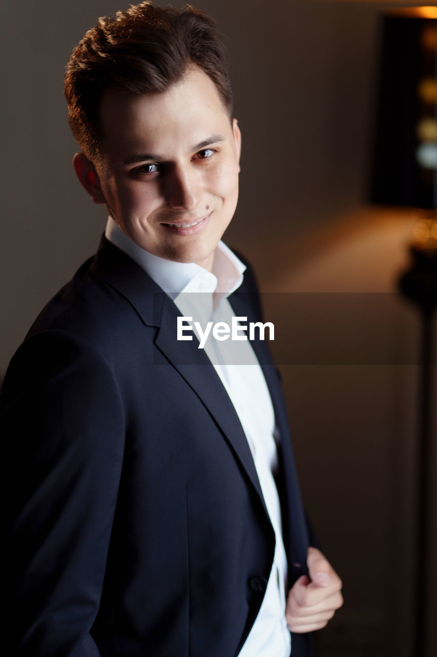 PORTRAIT OF YOUNG MAN STANDING AGAINST WALL