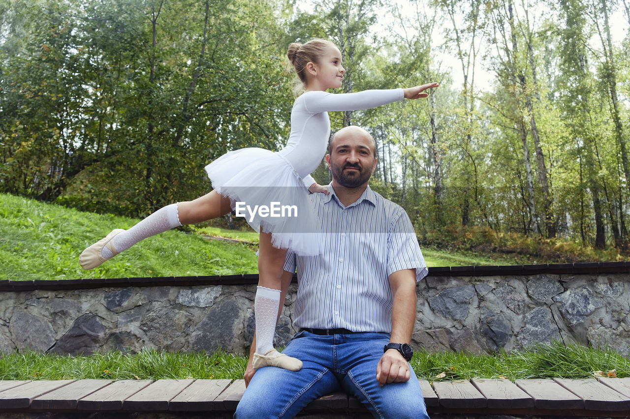 A little ballerina supported by her dad shows an element of ballet on a walk in the park