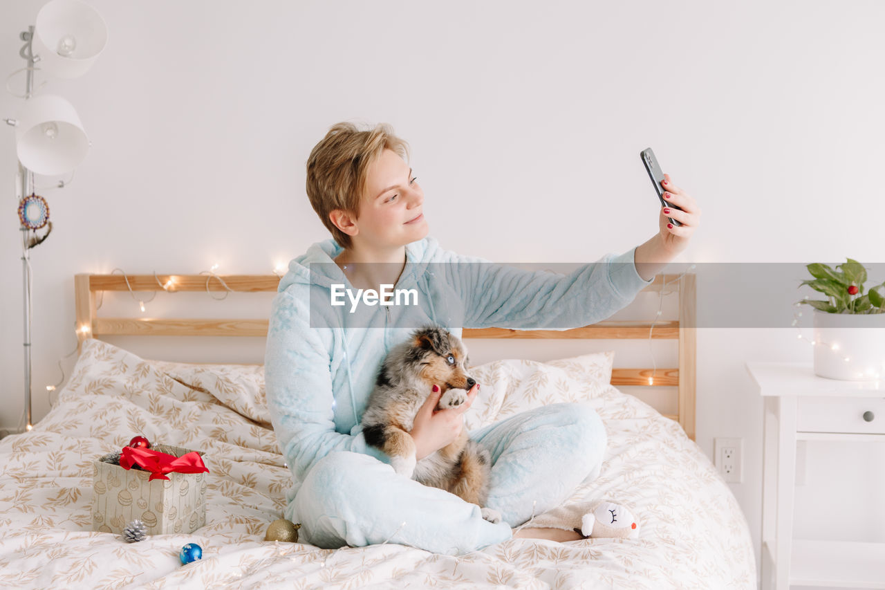 Woman taking selfie picture with cute puppy dog pet on smartphone. distant holiday celebration 