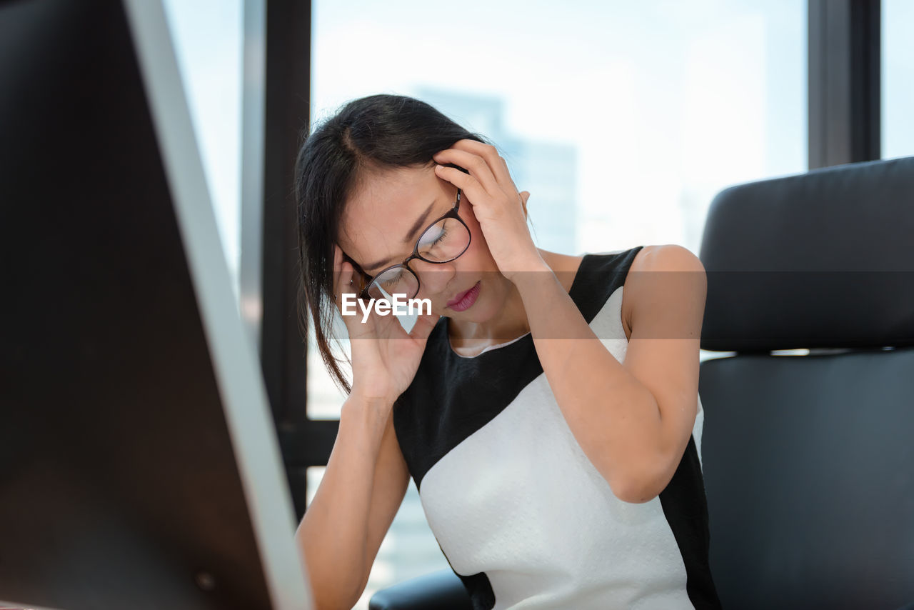 Woman with head in hand sitting on chair by window in office