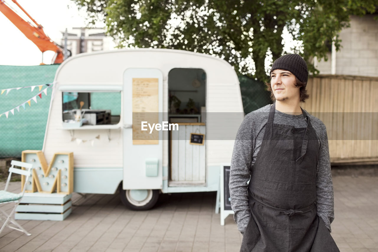 Thoughtful male owner looking away while standing outside food truck on street