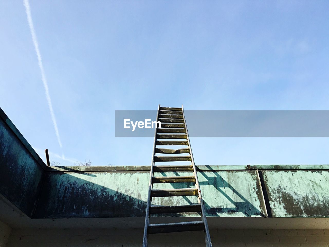 Low angle view of metallic ladder leaning on retaining wall against sky