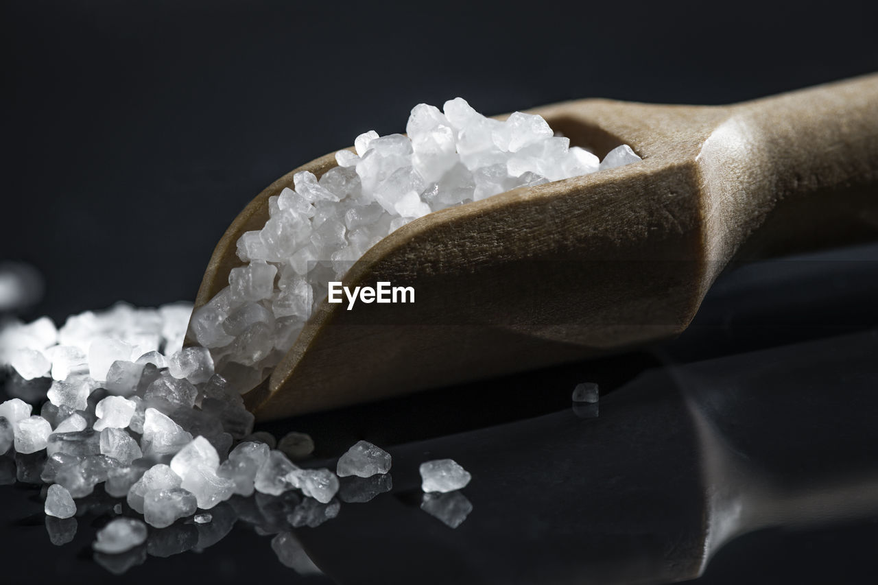 Close-up of sugar in wooden spoon against black background