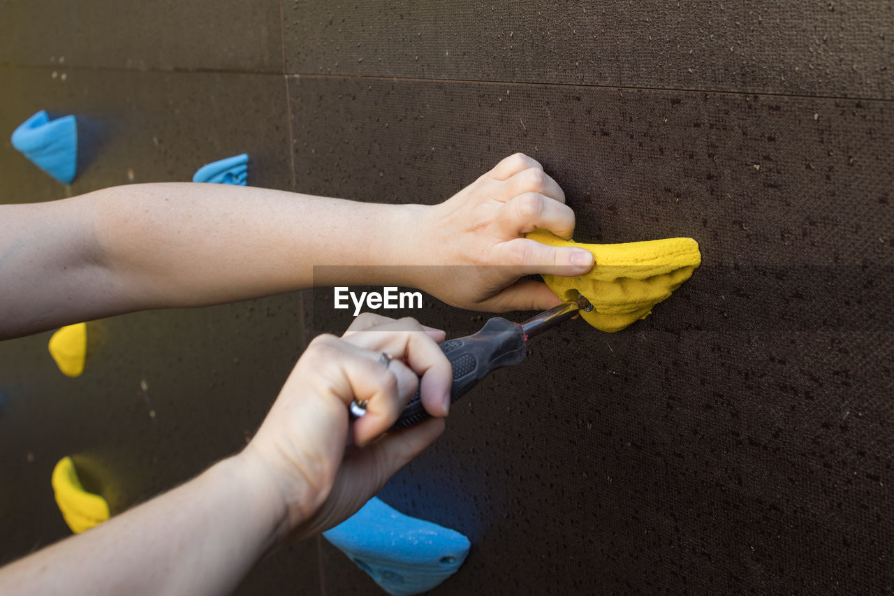 Anonymous crop worker with screwdriver fixing holds on climbing wall in modern gym