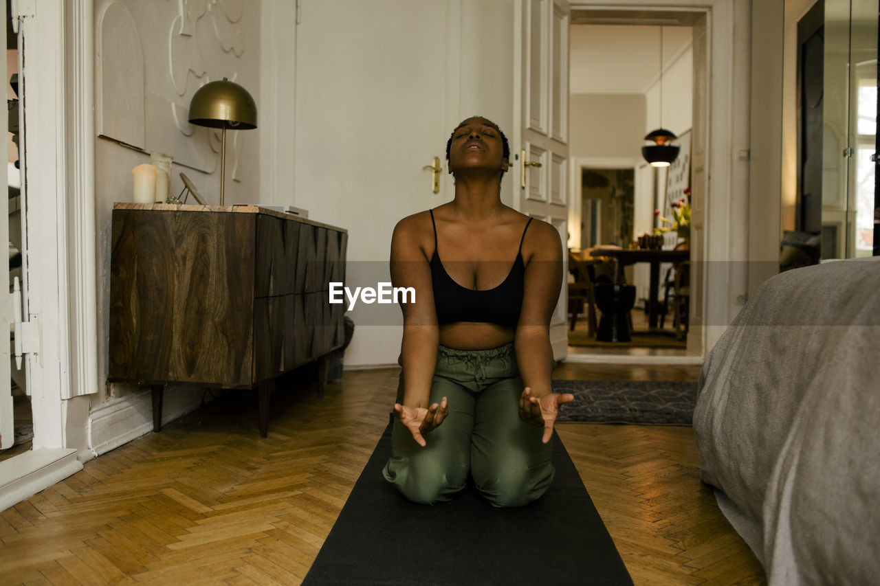 Young woman meditating on exercise mat at home