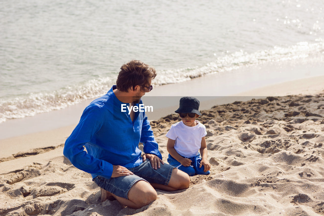 Dad and son play in sunglasses on the beach in summer in blue clothes while on vacation