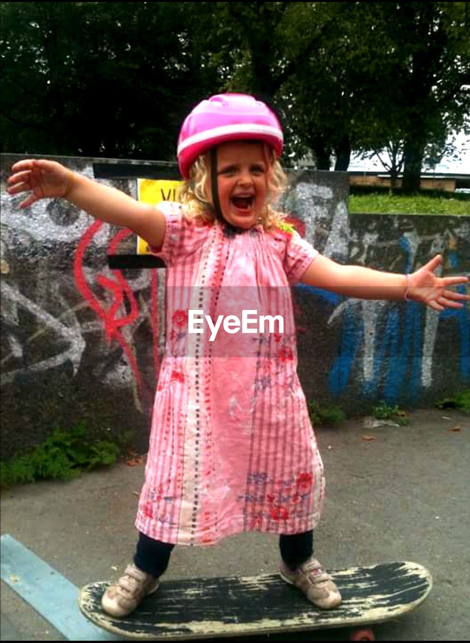 Full length portrait of cheerful girl skateboarding on footpath