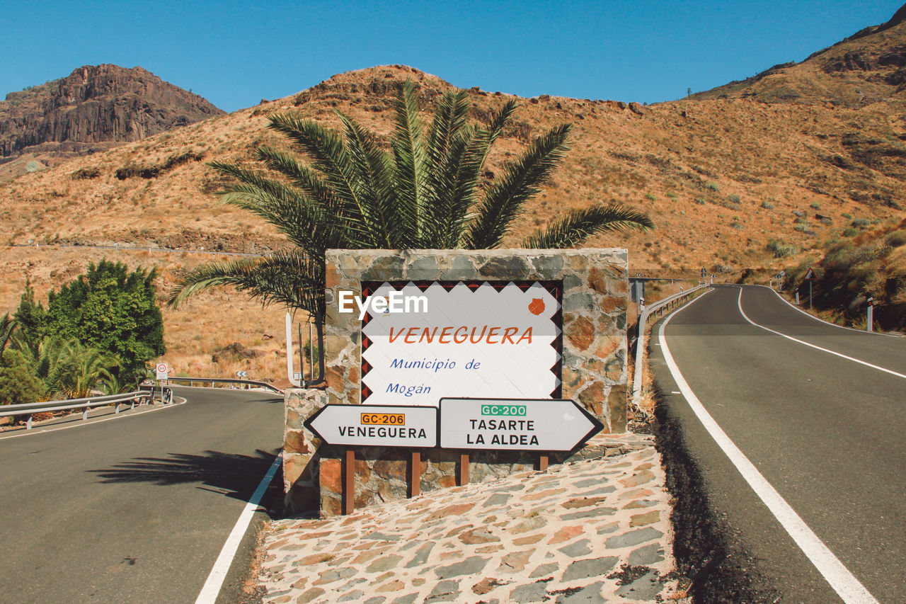 Road sign by mountains against clear sky