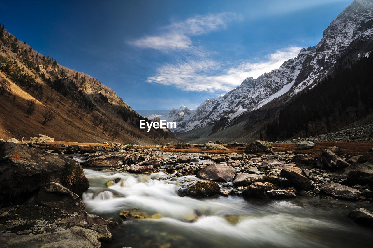 Stream flowing by mountains against sky