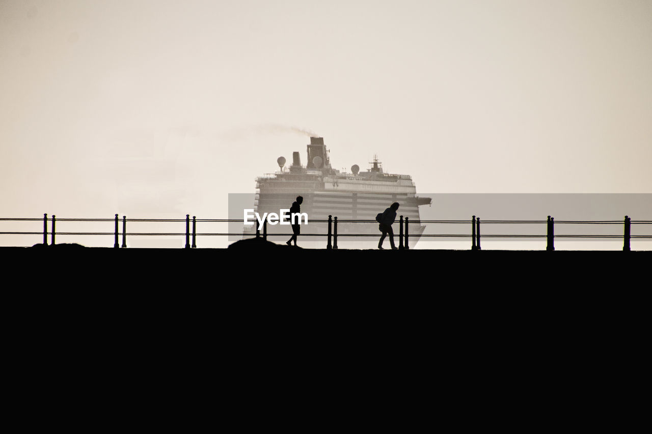 Silhouette people walking on bridge against clear sky