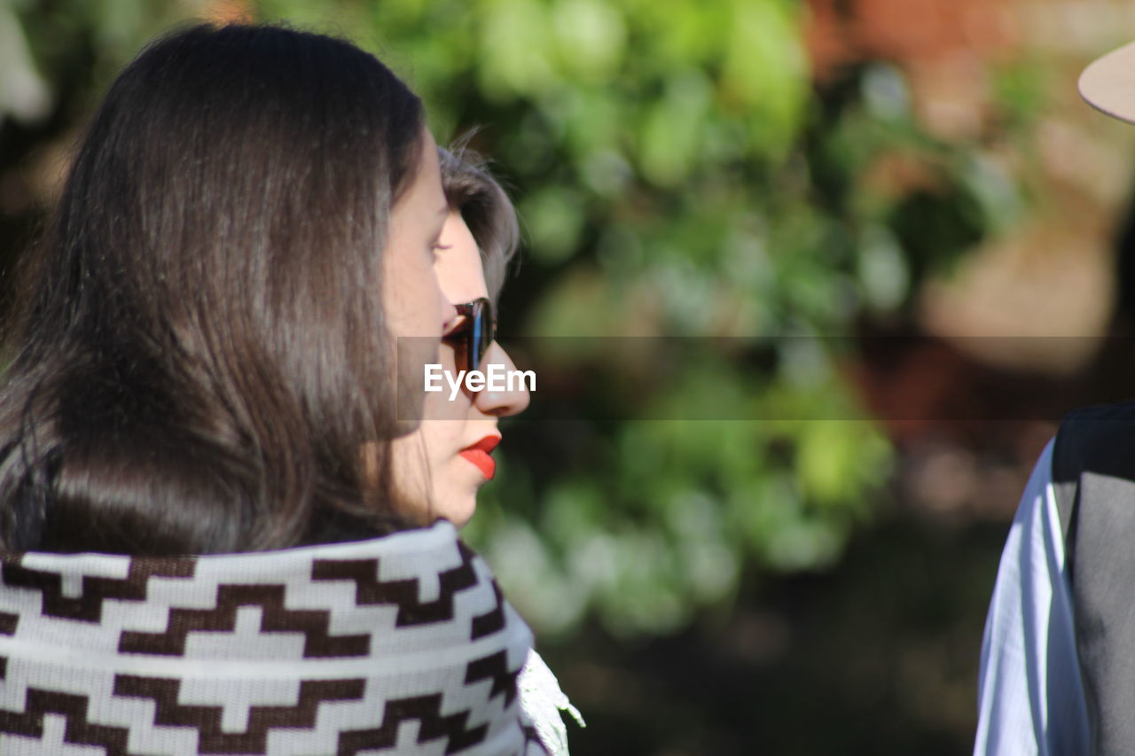 PORTRAIT OF YOUNG WOMAN STANDING AGAINST BLURRED BACKGROUND