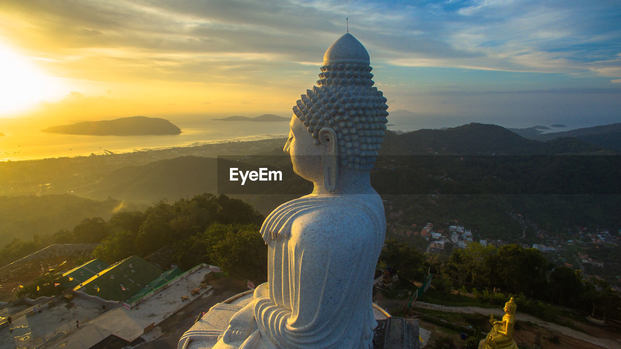 Tall buddha statue against cloudy sky during sunrise