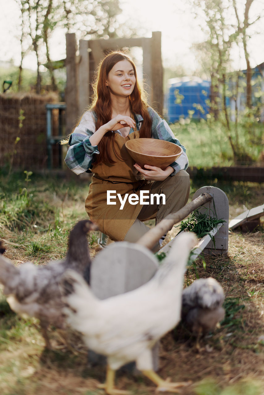 Happy female farmer feeding chickens at farm