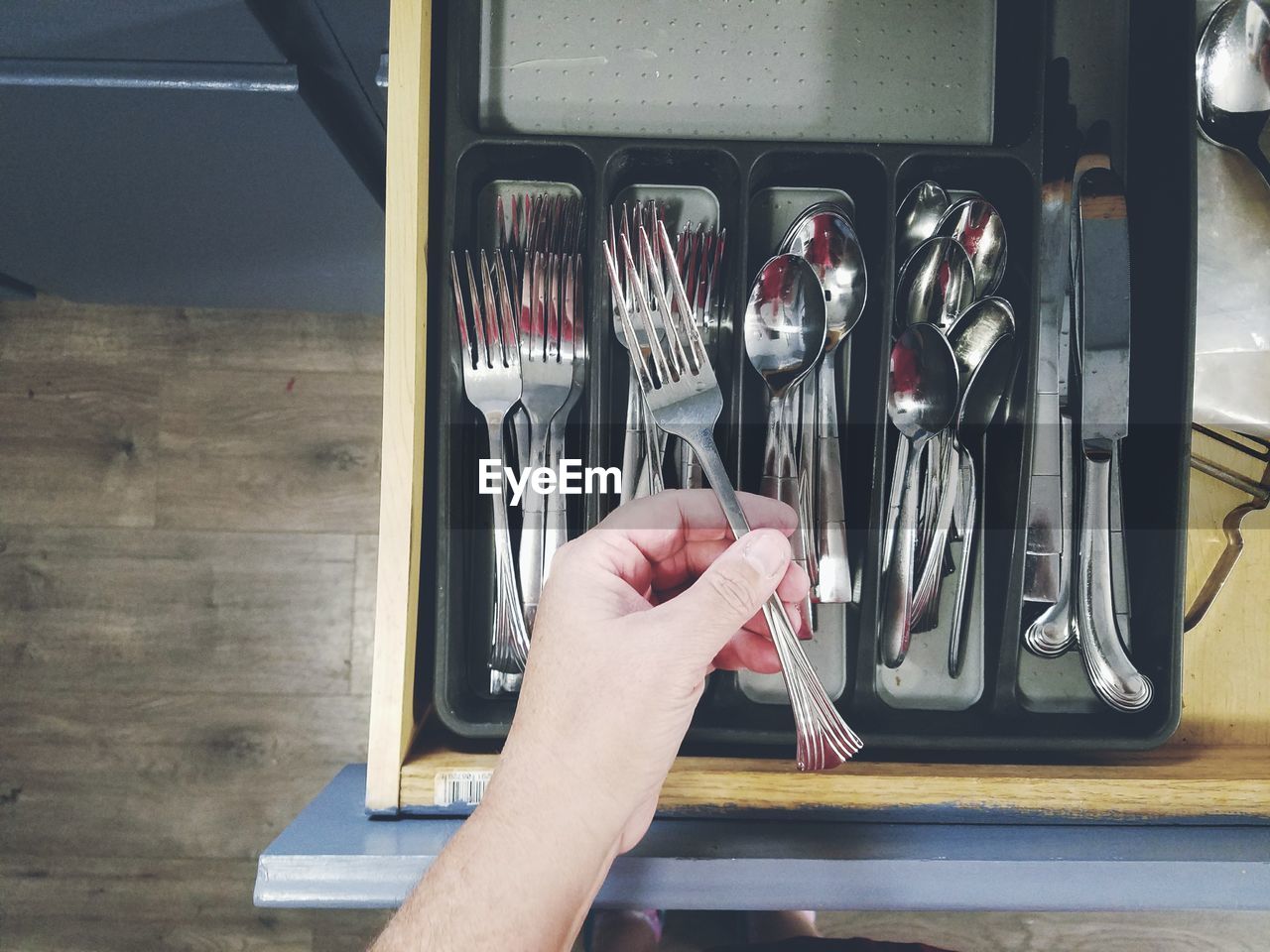 Cropped hand holding fork above drawer in kitchen