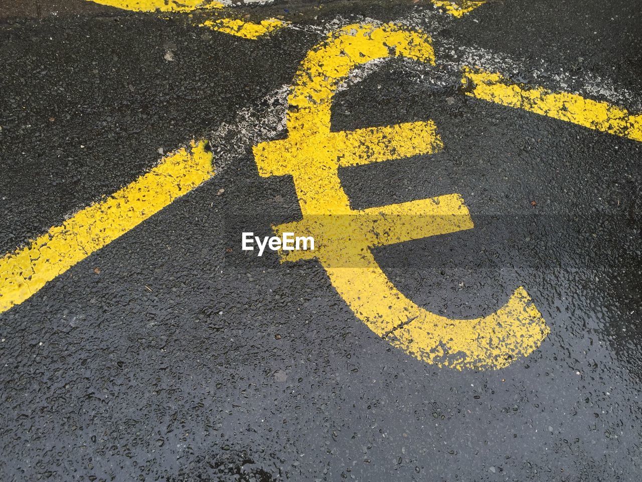 High angle view of yellow euro symbol on wet road