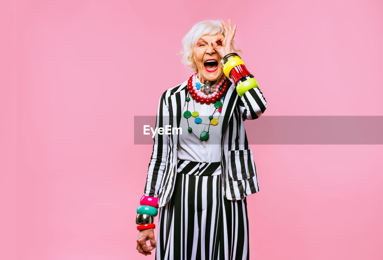 Portrait of senior woman screaming while standing against pink background