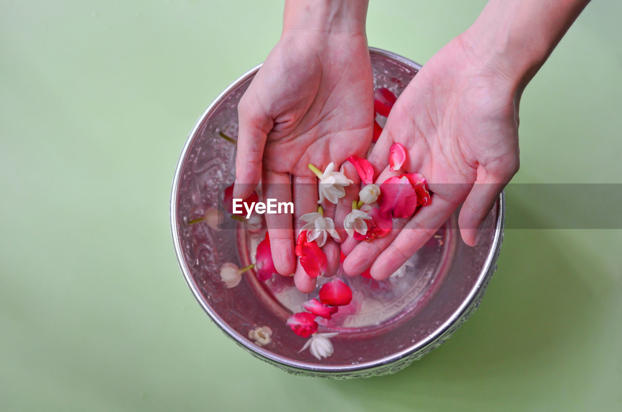 CLOSE-UP OF HAND HOLDING STRAWBERRY OVER BOWL AGAINST BACKGROUND