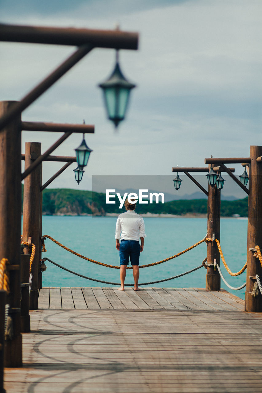 Rear view of man standing on pier over sea against sky