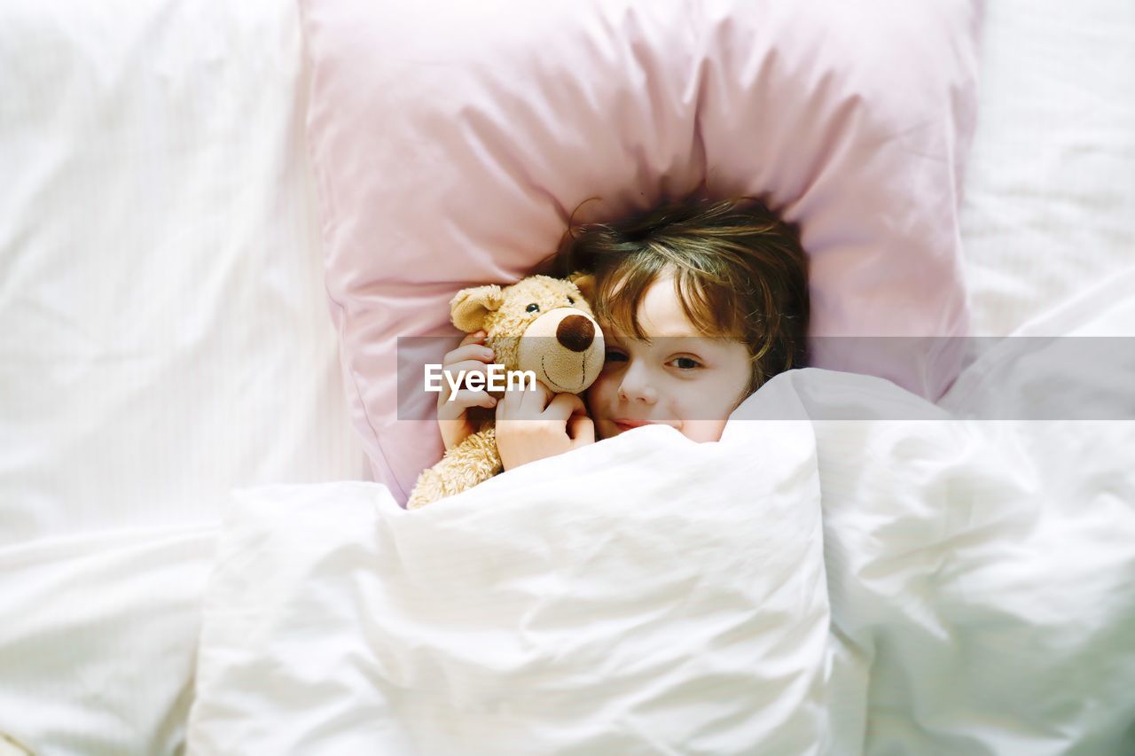 Directly above portrait of cute boy with teddy bear lying on bed at home