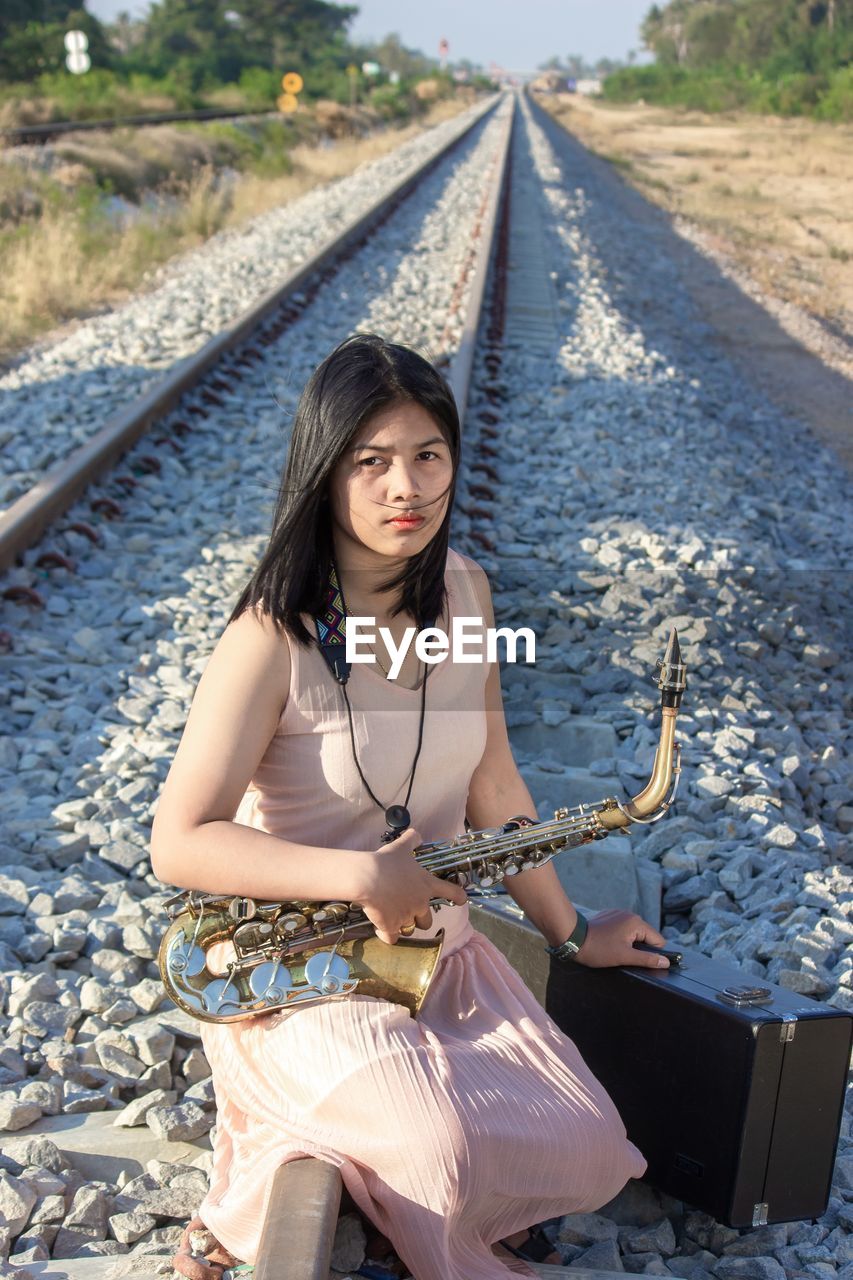 A saxophonist  woman sits on a railroad track to perform at a concert.