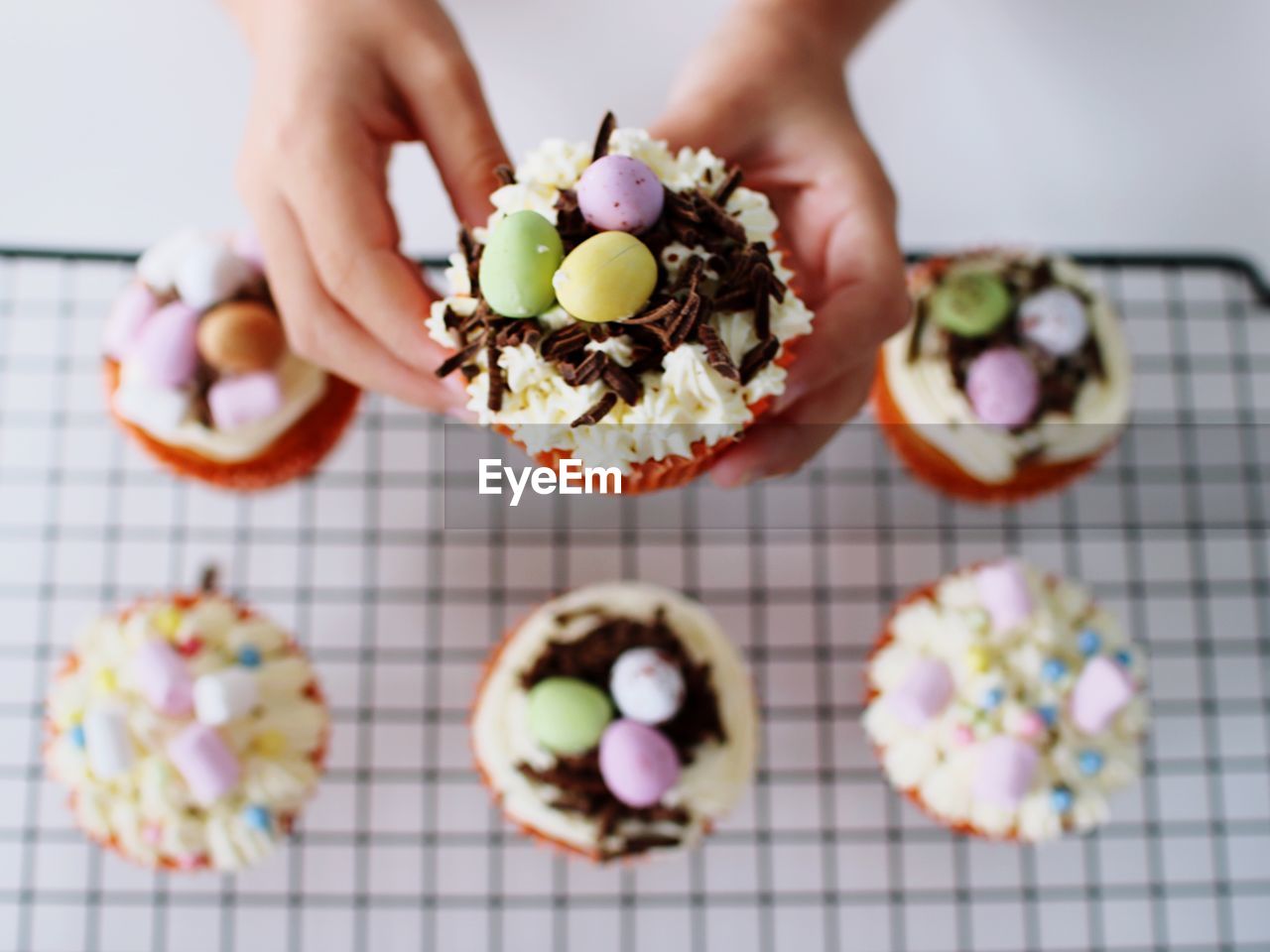 Cropped hands holding cupcakes on cooling rack at table