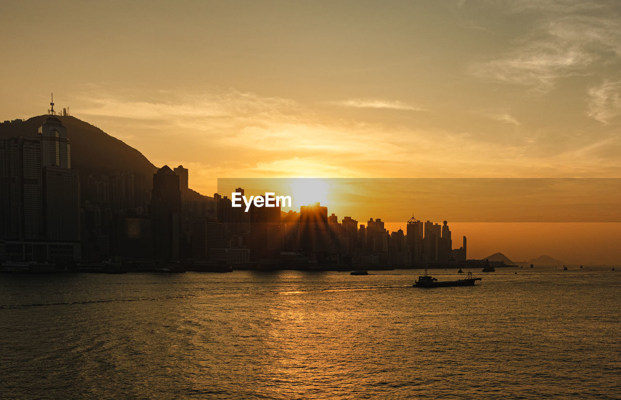 Silhouette buildings by sea against sky during sunset