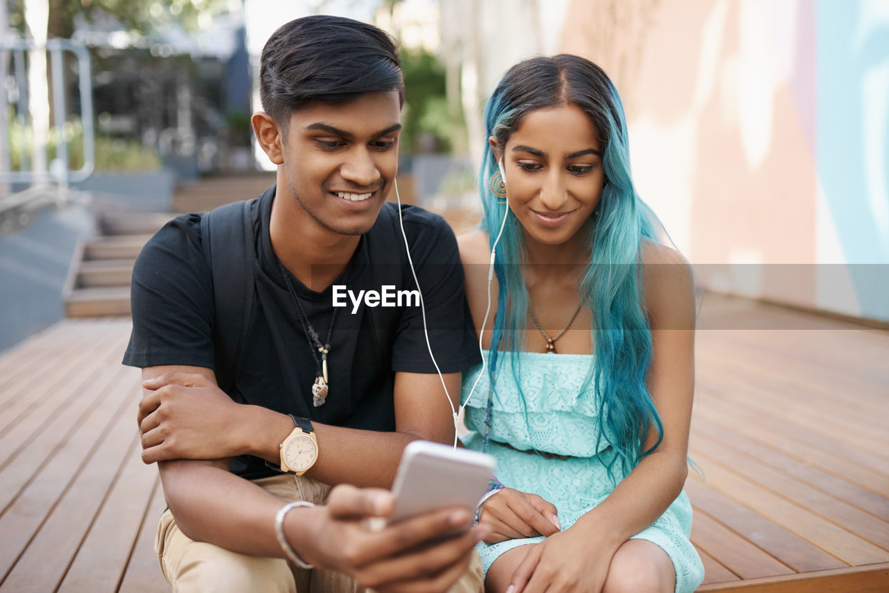 Happy friends using mobile phone while sitting outdoors