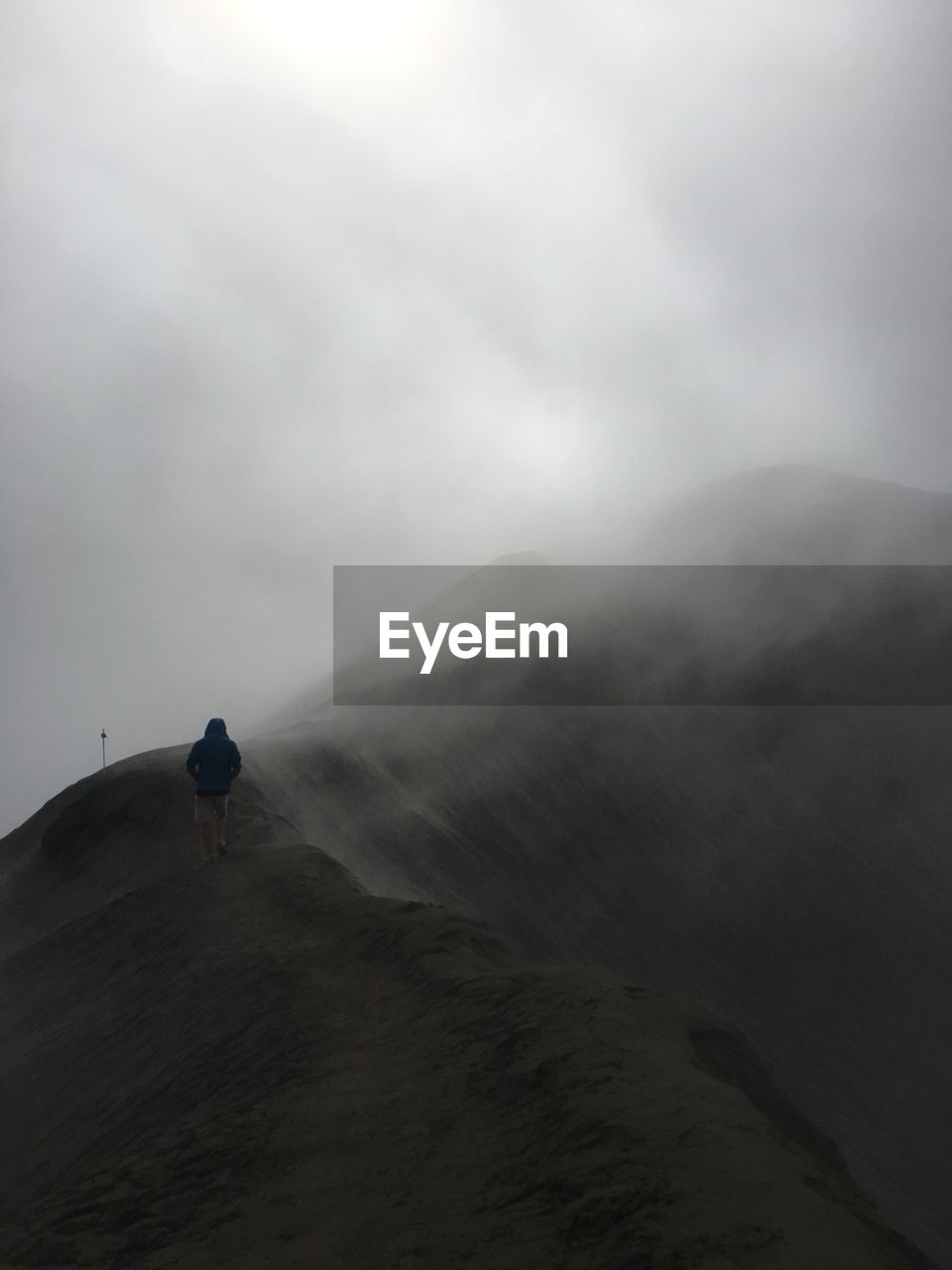 Rear view of man walking on mountain against sky during foggy weather