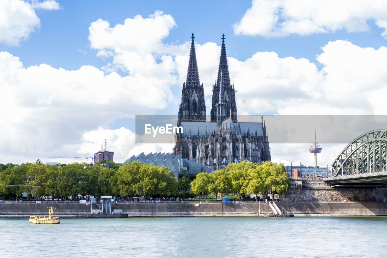 Scenic view of rhine river by cologne cathedral in city against sky