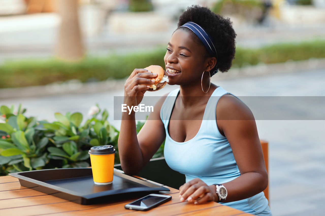 Cute african woman having lunch outdoors in city cafe. an african-american woman smiles