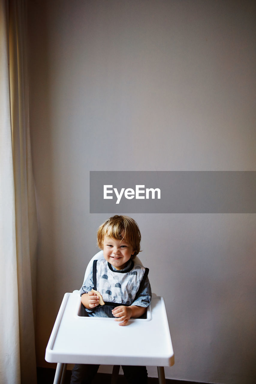 Cute boy sitting on table against wall