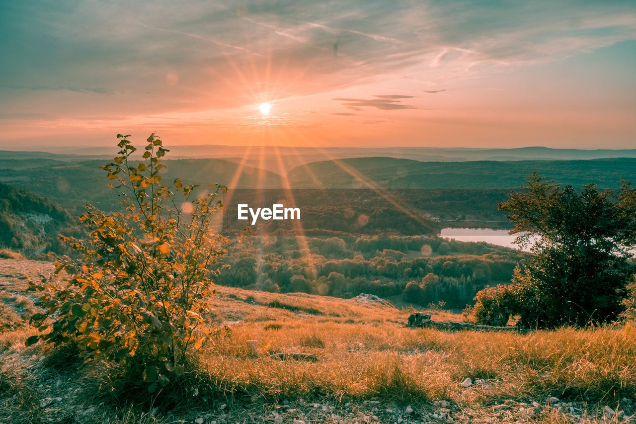 Sunlight streaming on landscape against sky during sunset