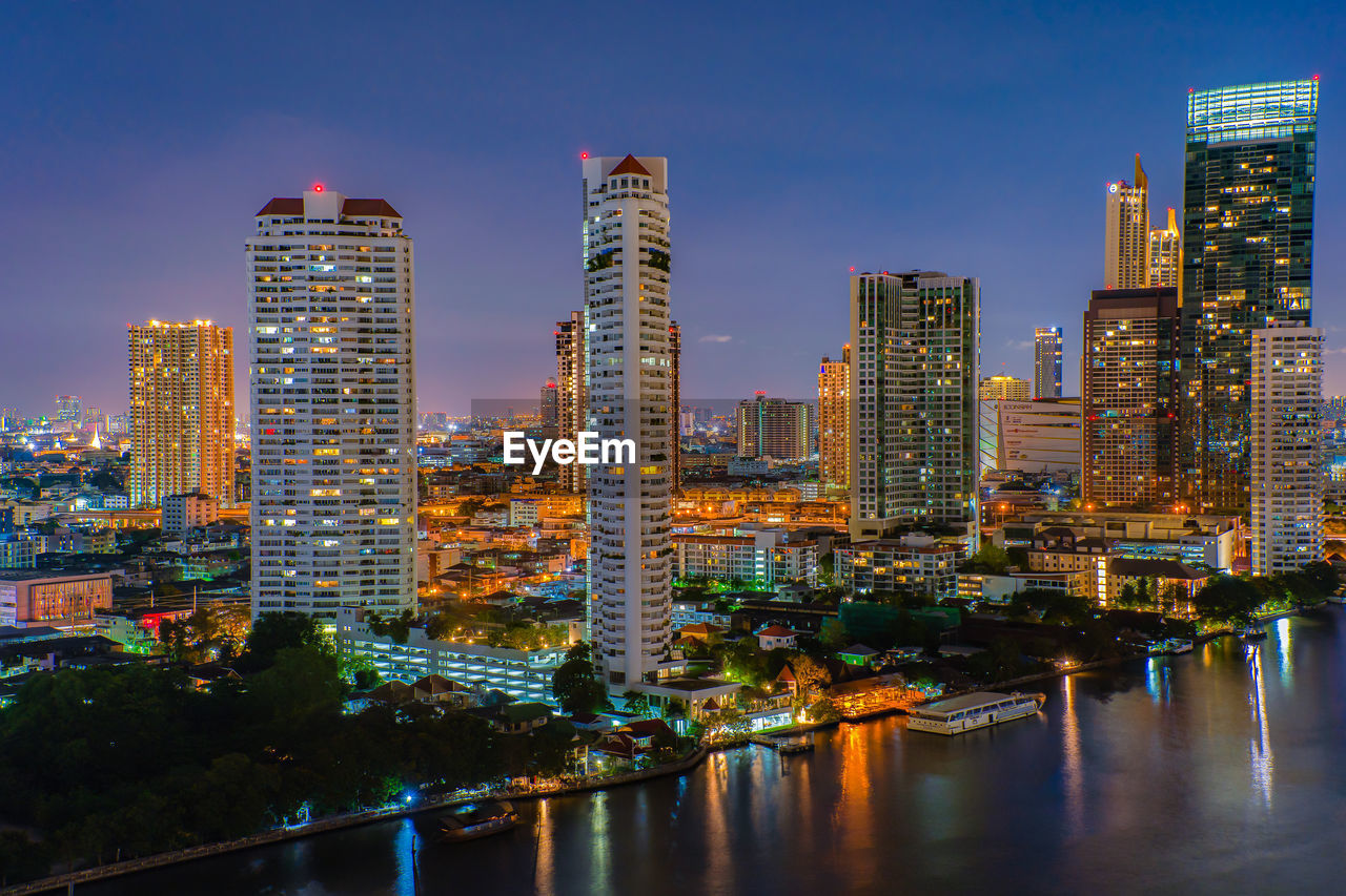 Illuminated buildings by river against sky in city at night