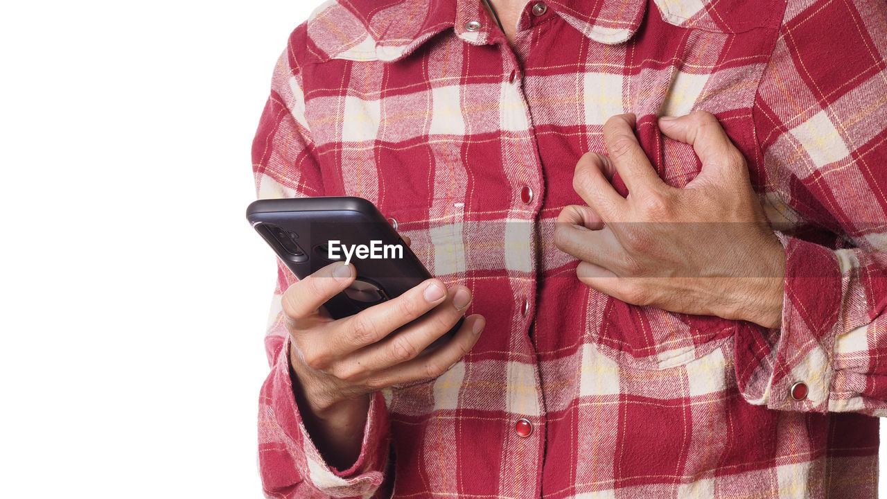 MIDSECTION OF WOMAN HOLDING MOBILE PHONE AGAINST WALL