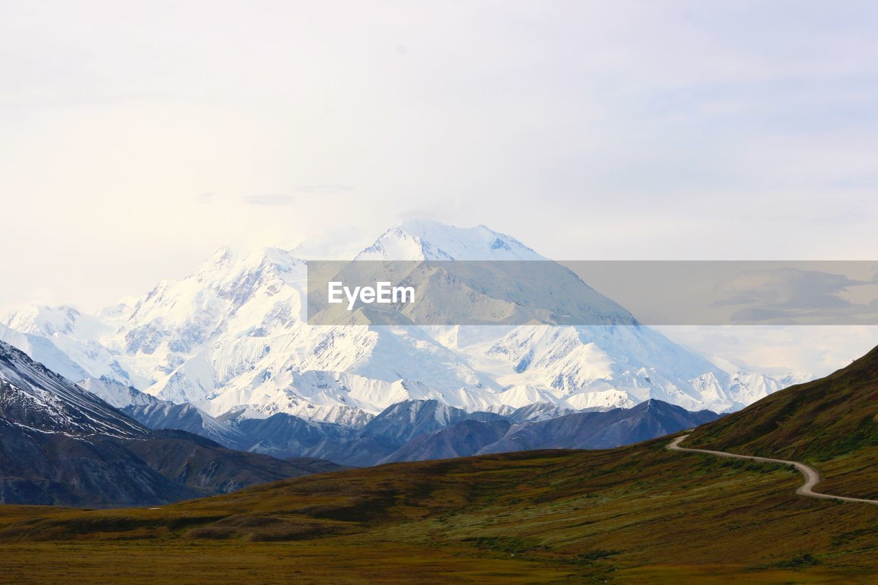 Idyllic shot of landscape against snowcapped mountains against sky