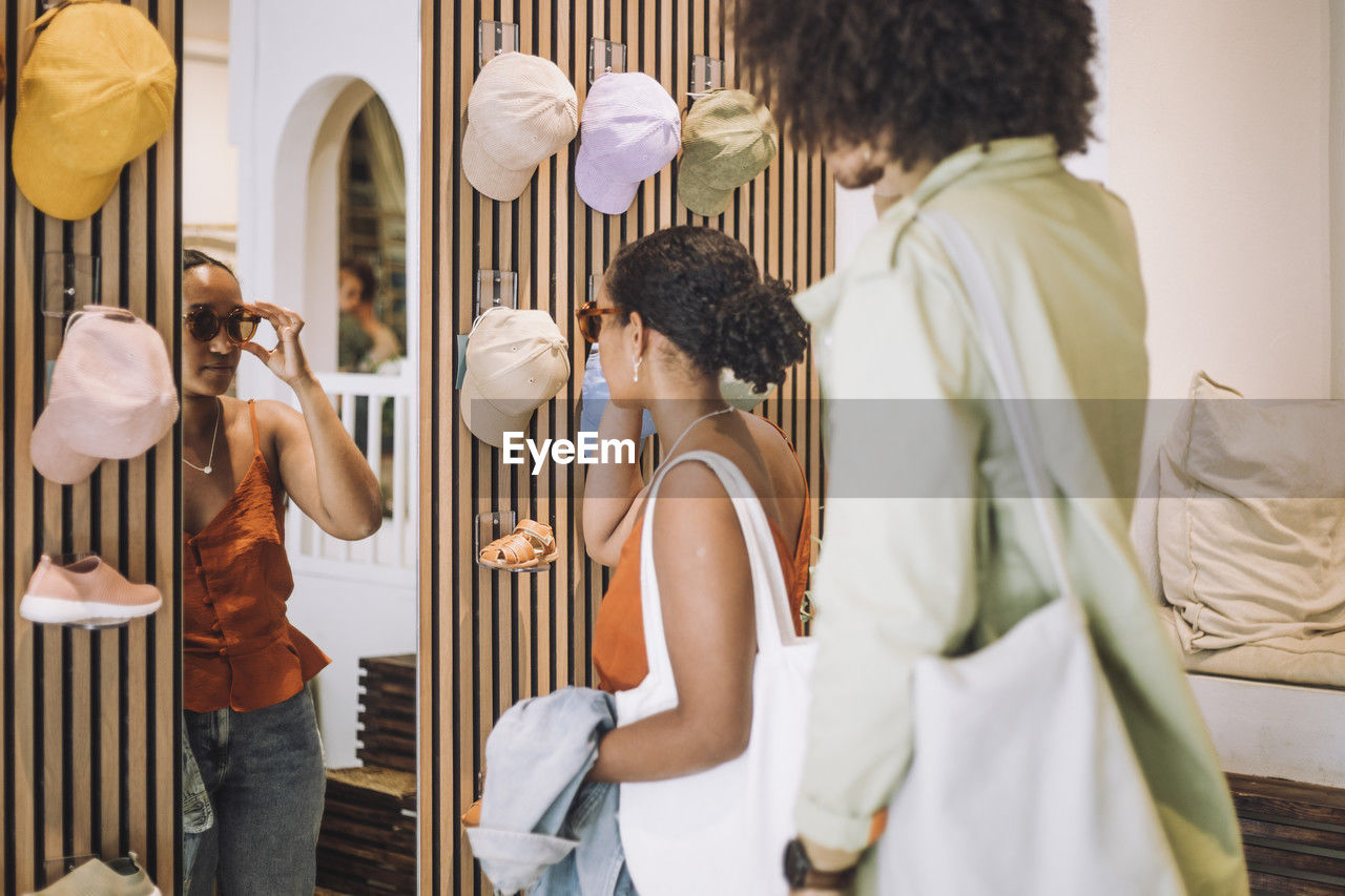 Woman trying sunglasses while standing by man at fashion boutique