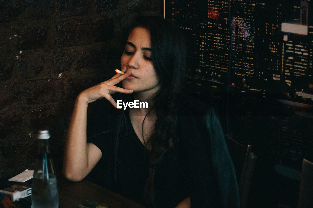 Young woman smoking cigarette while sitting at restaurant