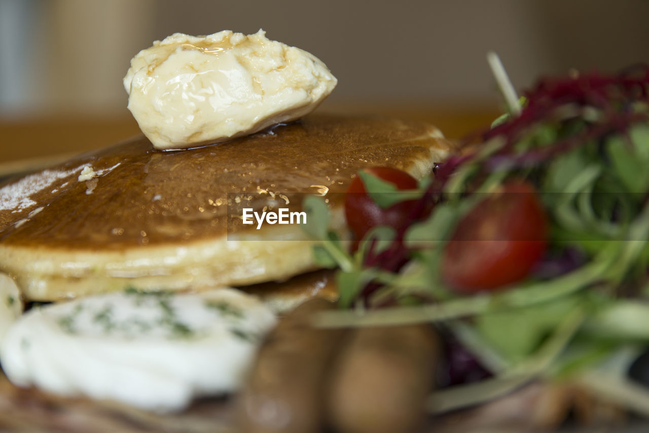 Close-up of pancakes with salad and poached egg in plate on table