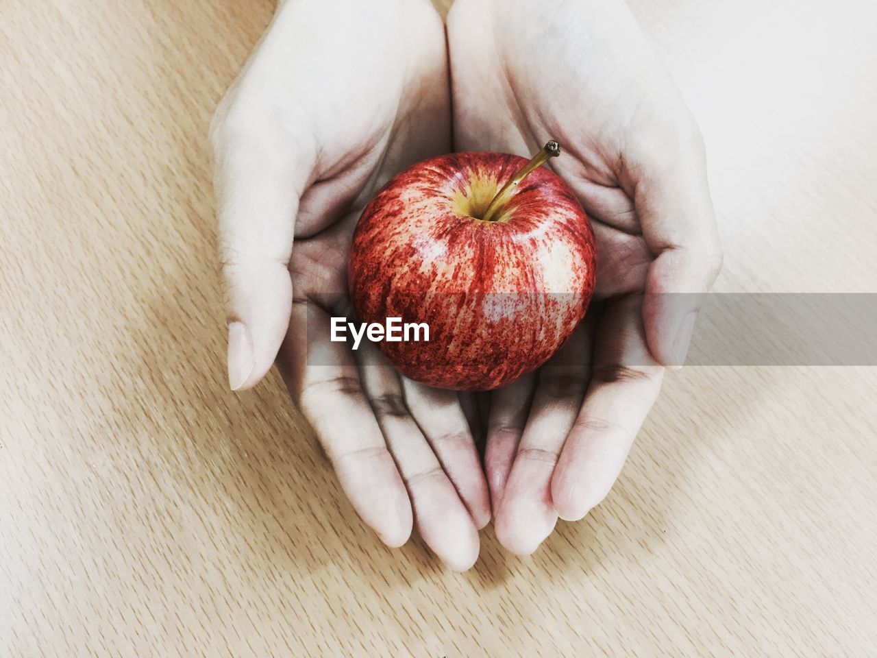 Close-up of cropped hand holding apple on table