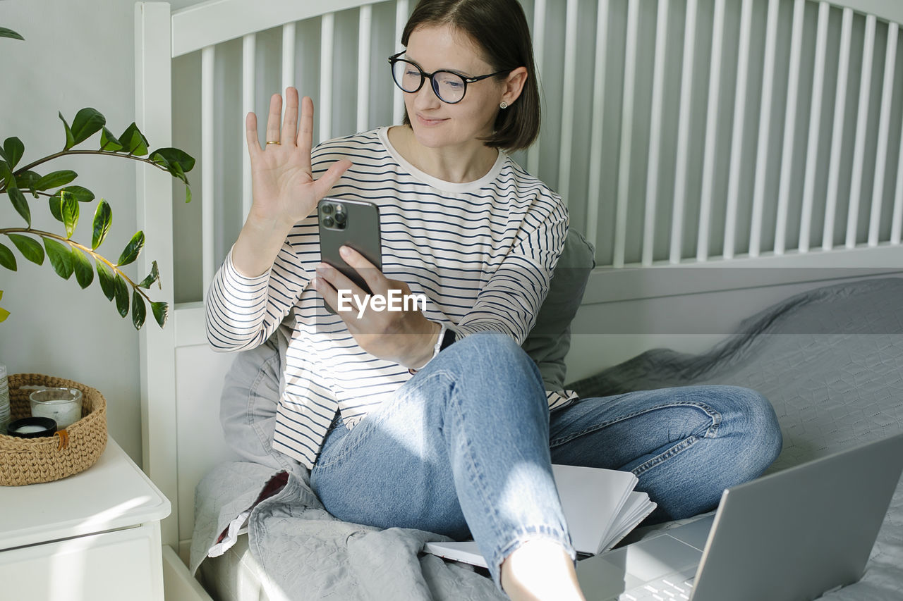 portrait of young woman using phone while sitting on sofa at home