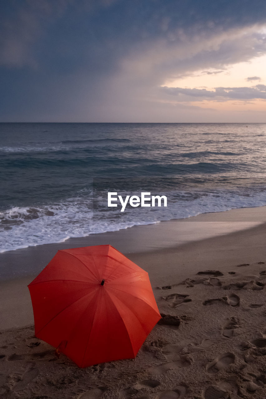 land, sea, beach, water, sky, protection, umbrella, horizon over water, horizon, nature, security, beauty in nature, cloud, sand, scenics - nature, red, ocean, wet, fashion accessory, wave, environment, sunset, coast, motion, storm, tranquility, holiday, summer, vacation, trip, parasol, outdoors, sports, rain, travel destinations, tranquil scene, wind, relaxation, body of water, no people, shore, sun, idyllic, coastline, sunlight, travel