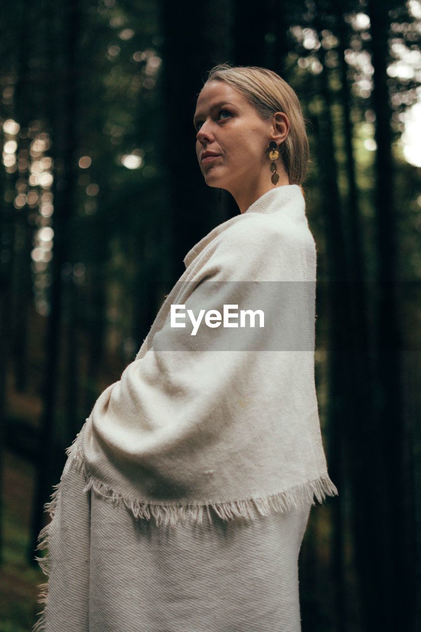 Young woman standing against trees in forest