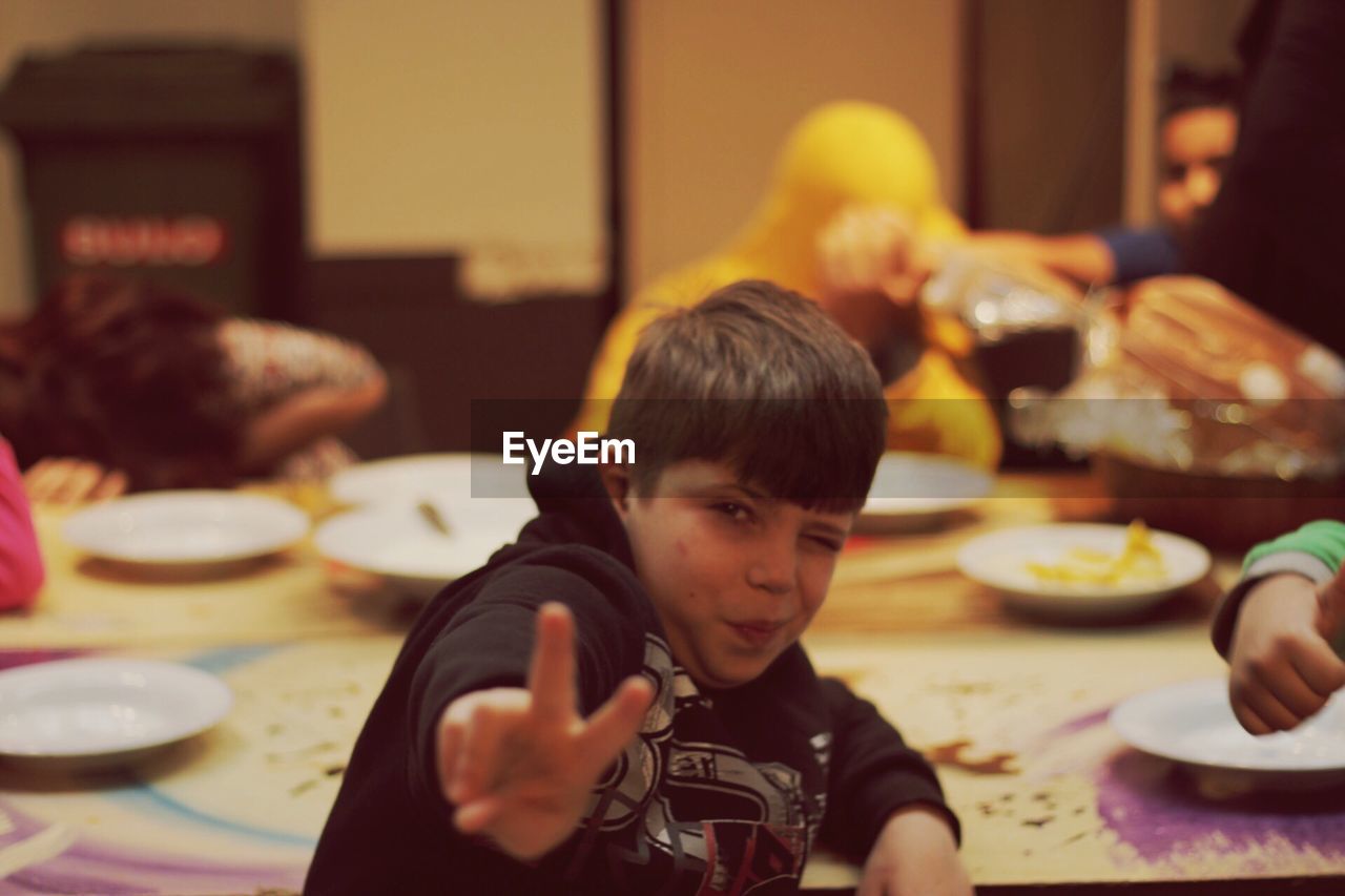 Portrait of boy doing peace sign by table at home