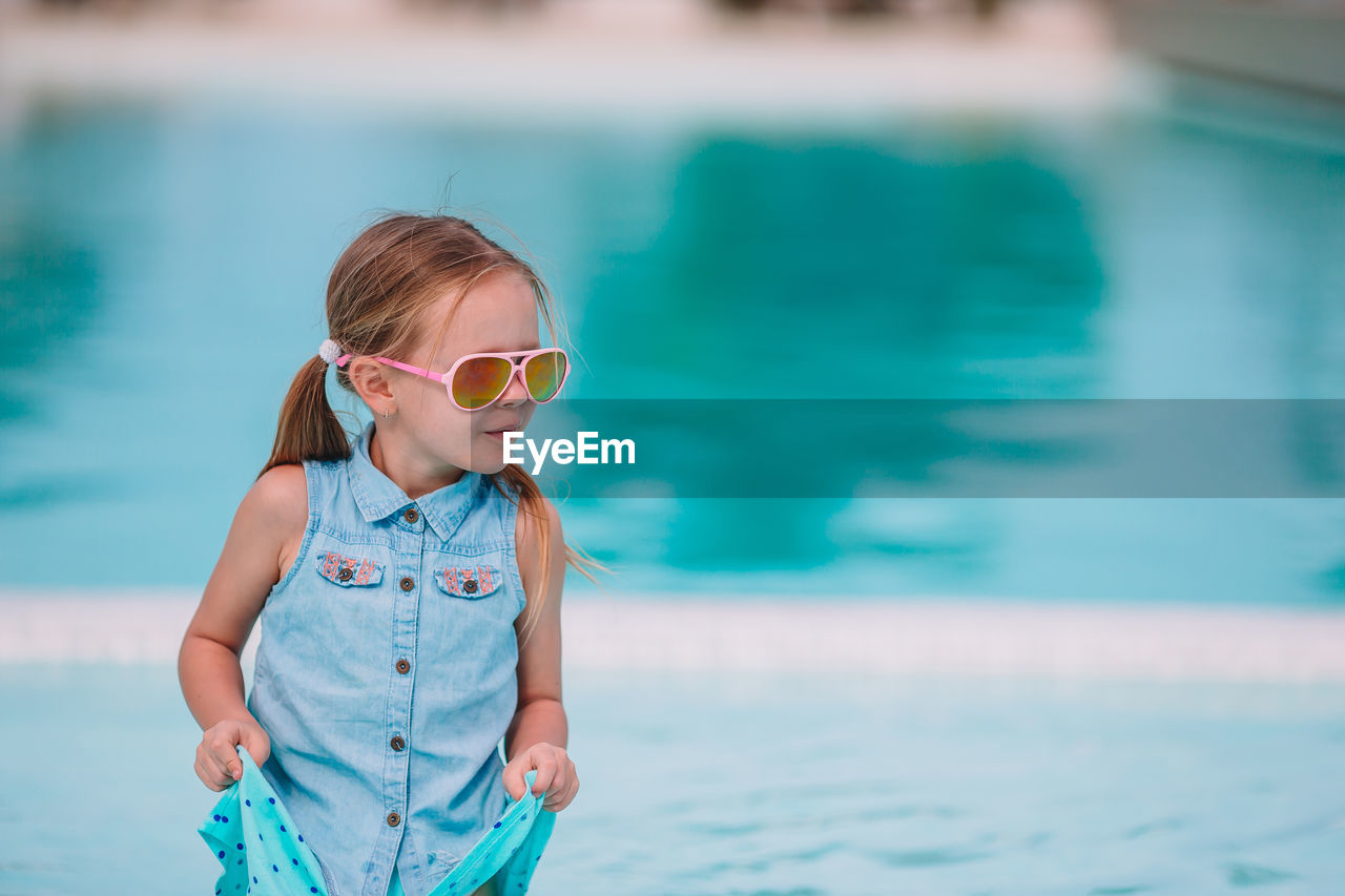 Cute girl wearing sunglasses against swimming pool
